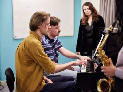 Music Therapy students in a class around a piano, one holding a saxophone